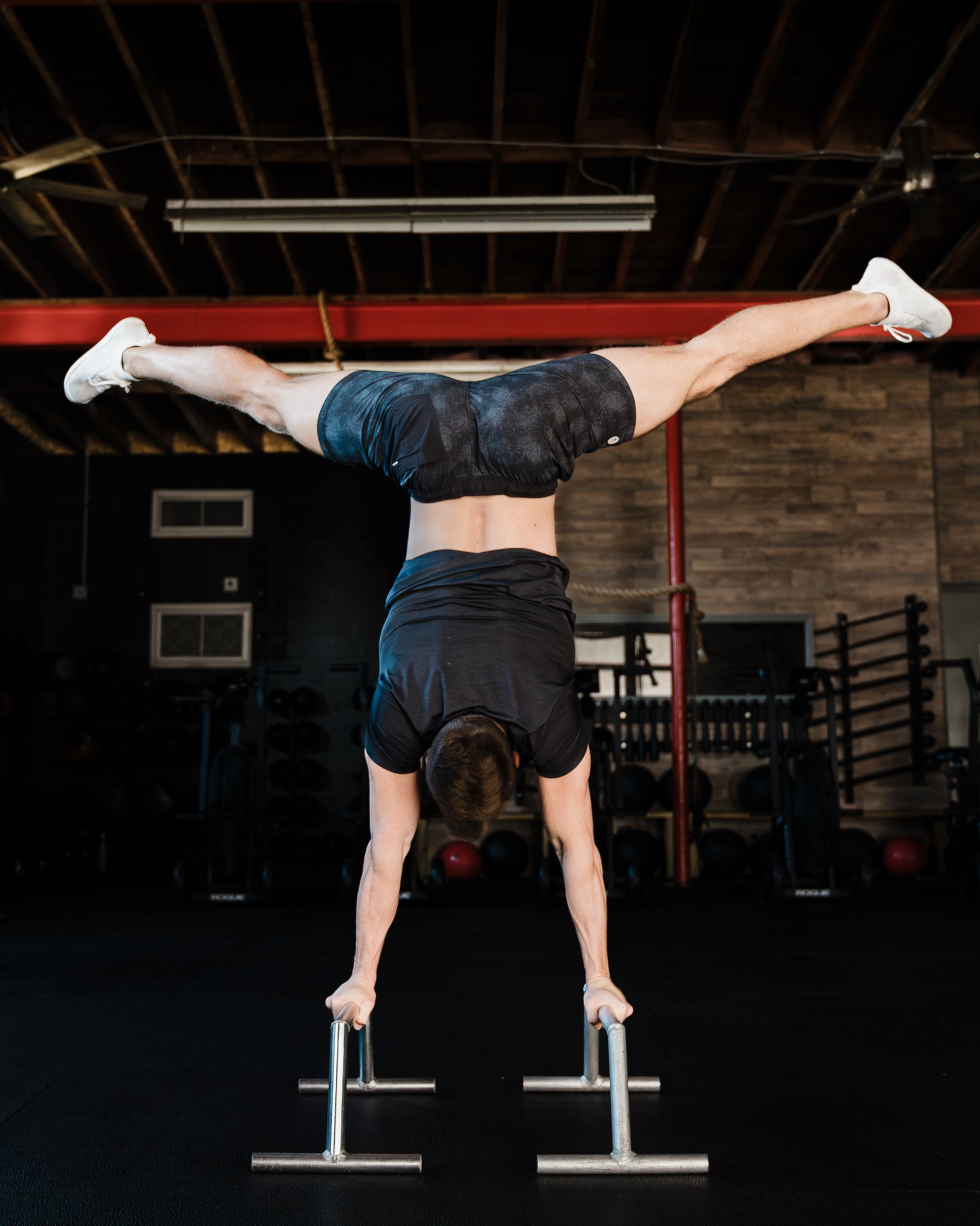 Dane demonstrating a straddle handstand on parallettes